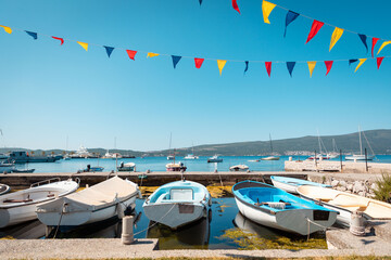 Beautiful sunny view of village pier with boats and flags on the Mediterranean coast. Summer...