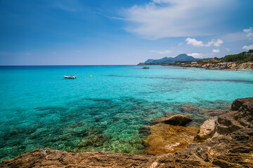 A beautiful clear turquoise Mediterranean sea with a lonely boat and rocks near the coast - a serene coastal scene from Mallorca