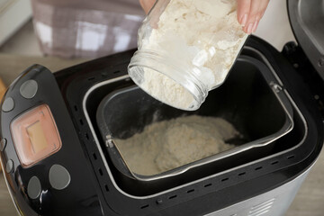 Making dough. Woman adding flour into breadmaker machine, closeup