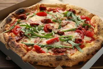 Tasty pizza with cheese, tomato and arugula in cardboard box on table, closeup