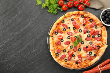 Tasty pizza with dry smoked sausages, olives, tomatoes, pepper and parsley on grey table, top view....