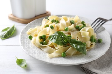 Delicious pasta with green peas served on white wooden table