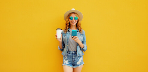 Summer stylish happy young woman with smartphone in straw tourist hat posing on yellow background