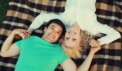 Portrait of beautiful happy smiling young couple in love lying together on a blanket, summer park