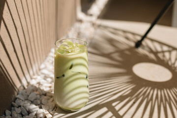 A glass of matcha latte with dappled light in the summer. Vacation, holiday, mocktail, summer bar...