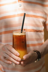 Man holding a glass of iced coffee with pineapple juice on a hot summer day outside.