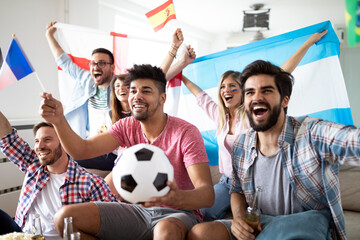 Diverse friends sports fans watching football match on TV at home. Celebrating shouting excited