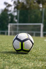 A close-up of a soccer ball placed on a green grass field with a goalpost in the blurred...