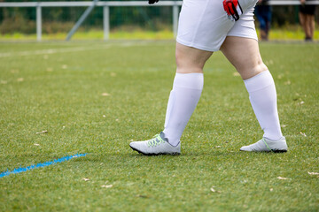 Obraz premium A partial view of a soccer player standing on a grass field with a focus on the legs and soccer cleats