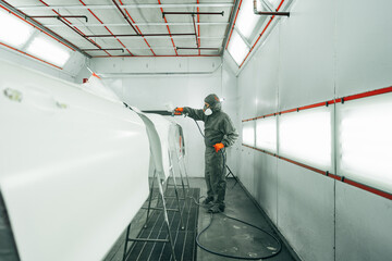 Auto painter painting a car with vaporizer gun inside a paint booth