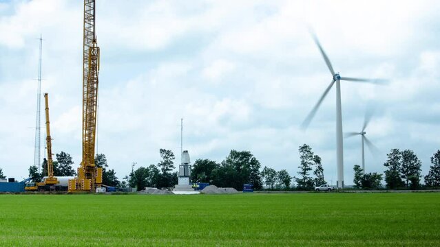 Timelapse of the construction of a windmill as windmills are spinning in the wind in the background.