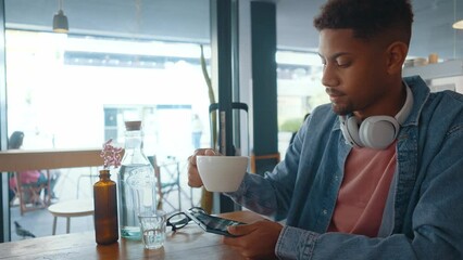 Cinematic image of a young man relaxing in a nordic styled cafe and enjoying his cappuccino while looking his digital tablet. - Powered by Adobe