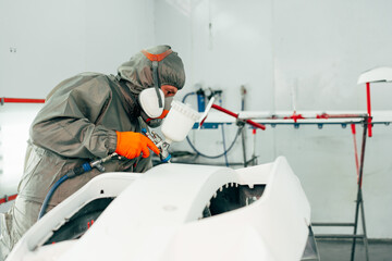 Auto mechanic worker wearing protective workwear spraying white paint on car part at workshop