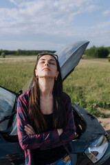 A young distressed beautiful lonely female driver stands near a broken down black car after an...