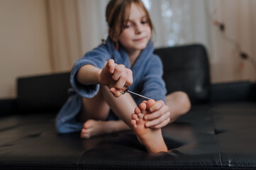 Girl, child sitting in the room on the sofa, cutting her toenails with manicure scissors. Close-up...