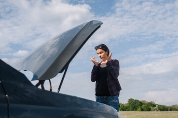 A young distressed beautiful lonely female driver stands near a broken down black car after an...