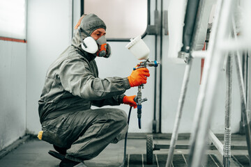 Auto painter painting a car with vaporizer gun inside a paint booth