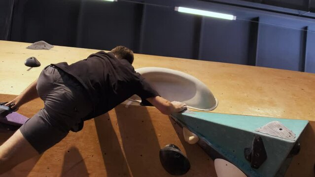 Man feet climbing on stone ledges at rock wall in sports center. Athlete gets up without safety harness slow motion low angle shot