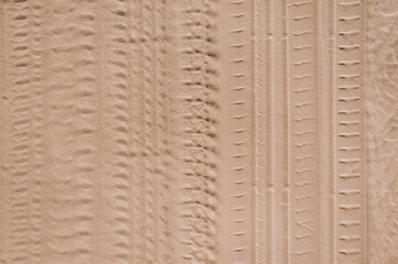 Background, texture of the uneven surface of traces, imprints from wheels, car tires on a sandy road. Photo, top view.