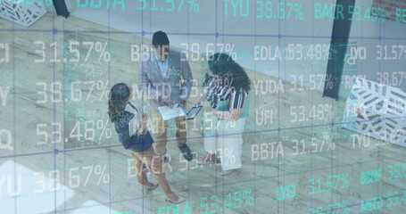 Image of trading board over high angle view of diverse coworkers discussing reports