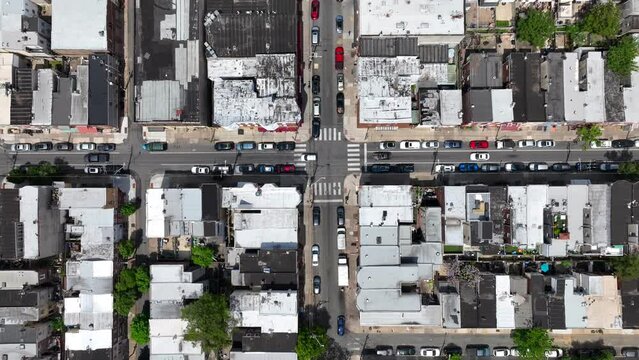 Busy urban intersection with dense row houses, parallel parking, and bustling traffic. Top down aerial above city housing neighborhood.