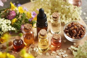 Many bottles of aromatherapy essential oil with myrrh, frankincense and colorful spring flowers