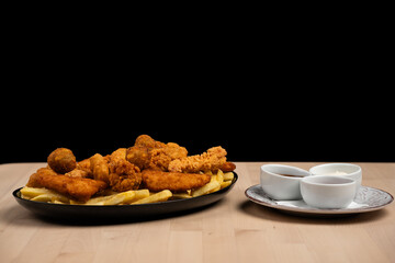 Close-up of chicken wings and fries served on a black plate with assorted dipping sauces