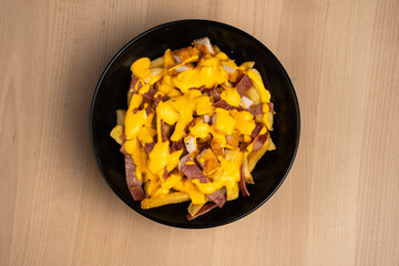 Top view of a black bowl on a wooden table filled with ham and cheese