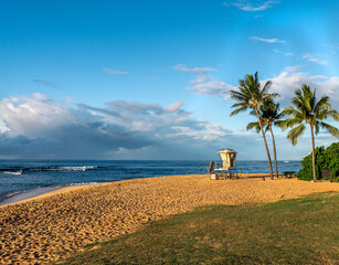 A white lifeguard shake guarding a swimming beach with coconut trees and grass by a clean blue ocean, Poipu Beach, Kauai