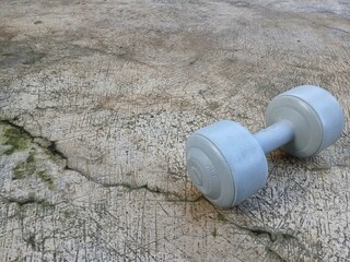 A gray dumbbell weighing 5 kg for exercise placed on the cement floor in the front yard of the house