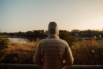Person seated on a wooden fence gazing at water.