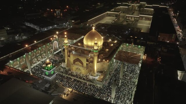 Drone shot of Imam Ali Holy Shrine in Iraq during prayer, capturing the serene ambiance, worshippers gathered, and intricate architecture bathed in soft light