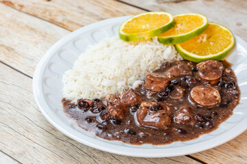Traditional Brazilian feijoada served with white rice and fresh citrus slices on a rustic wooden table, showcasing a hearty and flavorful meal.