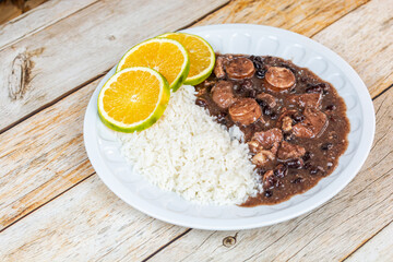 Delicious Brazilian feijoada served with white rice, sausages, and orange slices on a rustic wooden table.