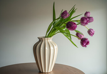 Bouquet of purple tulips in a cream vase on a wooden table
