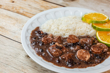 Traditional Brazilian feijoada served with rice and orange slices on a rustic wooden table, showcasing a hearty and flavorful meal.