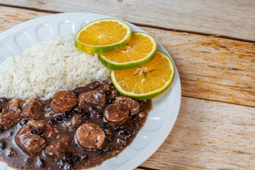 Traditional Brazilian feijoada served with white rice and garnished with orange slices on a rustic wooden table.