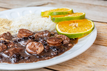 Traditional Brazilian feijoada served with rice, oranges, and farofa on a white plate. A savory and delicious cultural dish.