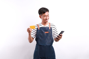 Young asian man barista barman employee wear blue apron work in coffee shop using mobile cell phone credit bank card shopping online isolated on white background