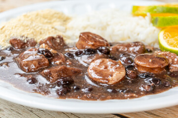 Traditional Brazilian feijoada served with rice, orange slices, and farofa on a white plate, showcasing rich colors and textures of a comforting meal.