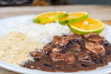 Delicious Brazilian feijoada served with rice, oranges, and farofa on a white plate, a traditional hearty black bean stew with pork.