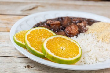 Delicious Brazilian feijoada served with rice, orange slices, and farofa on a rustic wooden table, showcasing traditional flavors.