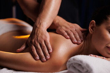 A young brunette woman receives a professional back massage in a spa salon. A beautiful naked lady in a towel with perfect skin gets a relaxing massage. The concept of luxury professional massage.