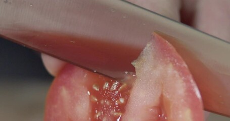 Super-closeup footage of adult hands cutting tomato piece with sharp knife, with blur background