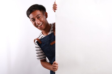 Funny happy joyful asian man in blue apron peeking behind the wall