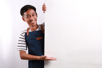 Cheerful Asian man in apron presenting something on white advertisement board on white background