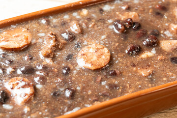 Close-up of traditional Brazilian feijoada with sausages and beans in a clay pot, showcasing rich textures and hearty ingredients.