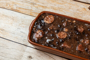 Traditional Brazilian feijoada, a hearty black bean and pork stew, served in an earthenware dish on rustic wooden table.