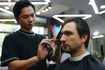 Barber cutting bangs of client with styling scissors