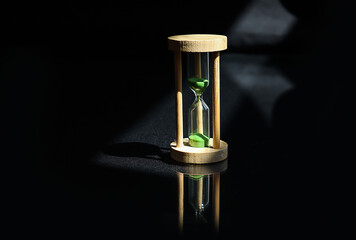 Concept of fast passage of time: hourglass on a black background in the rays of the sun, shadows...